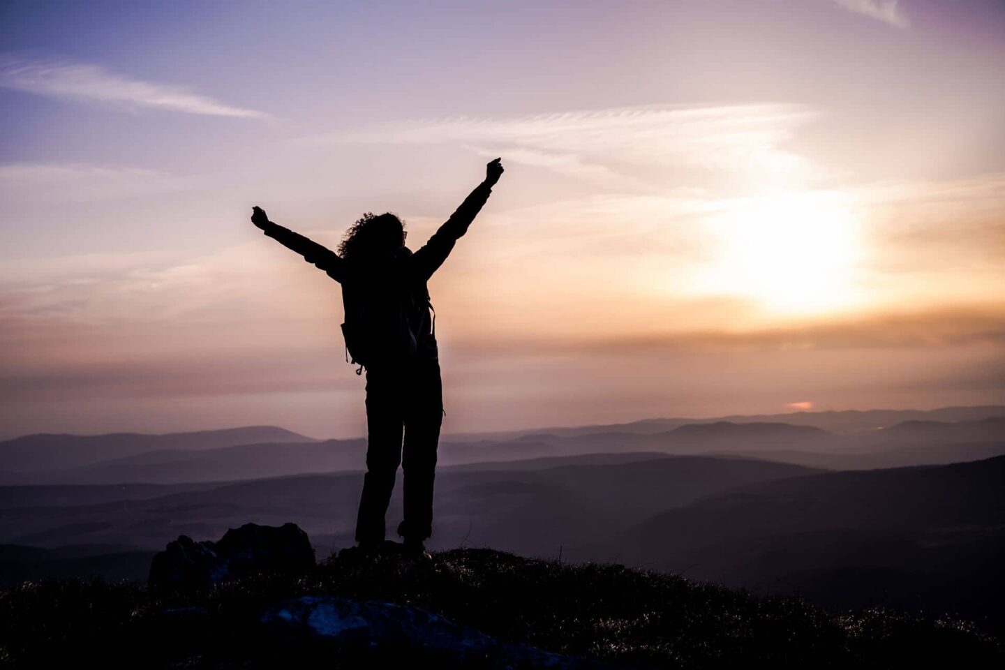 Hiker watching sunset with arms raised in victory