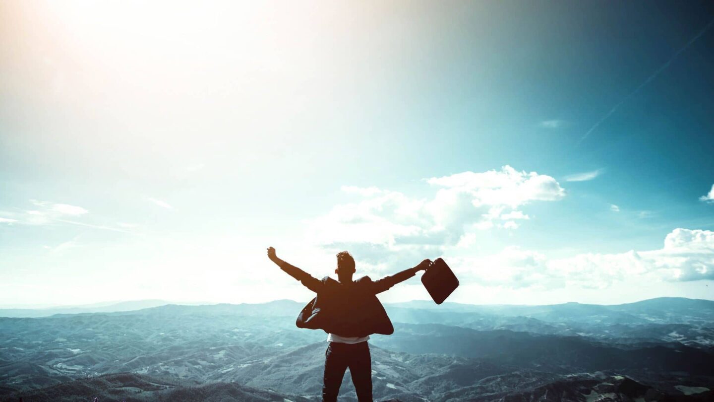 Man raising arms in victory standing on a mountain top with his briefcase